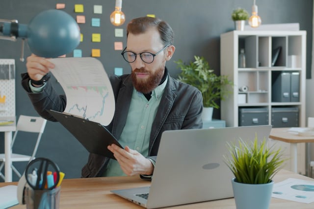Reviewer examining printed charts beside a computer